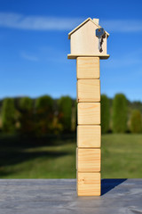 Wooden house model with key on six blank cubes on green blurred landscape and blue sky background with copy space. House building, loan real estate or buying or renting new home concept.