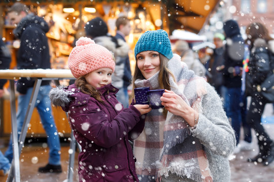 Happy kid girl and young beautiful woman with cup of steaming hot chocolate and mulled wine. Adorable child and beautiful mum on Christmas market in Germany. Family walking on Xmas market.