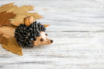 Autumn crafts. Children's fall crafts and creativity, Hedgehog made from modeling clay, sunflower seeds and nuts, on dry yellow leaves. Ideas for children's art
