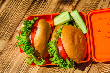 Hamburgers with lettuce in lunchbox on wooden table. Top view
