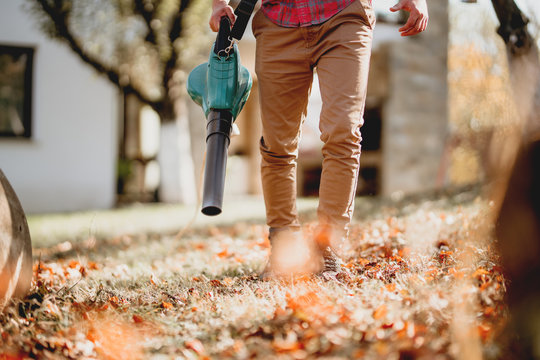 Autumn cleaning in backyard. Close up details of worker using leaf blower, garden blower and vacuum