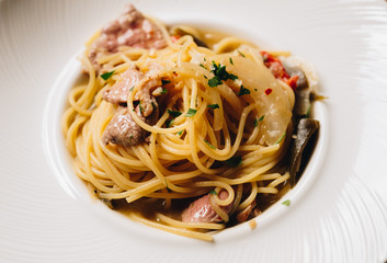 Spaghetti spicy with bacon, dry chili, green olive in white dish top view on wooden background. 