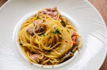 Spaghetti spicy with bacon, dry chili, green olive in white dish top view on wooden background. 