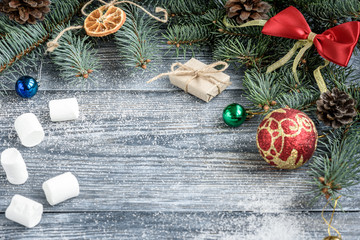 Christmas or New Year decoration background with fir branches, cones, balls, marshmallows on grey wooden board.