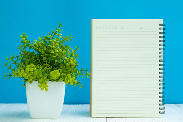 Blank notebook on white wood table front blue wall background with copy space for add text or advertising word.