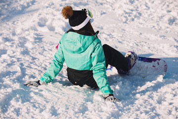 Fototapeta na wymiar Leisure, sport concept - woman snowboarder sitting on snow