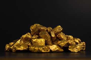 Fototapeta premium A pile of gold nuggets or gold ore on black background, precious stone or lump of golden stone, financial and business concept.