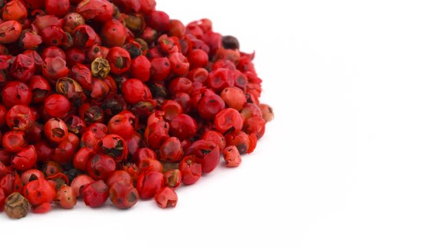 Quarter of circle shaped pink pepper peppercorn pile in the left top corner of the frame. Rotating. Isolated on the white background. Close-up. Macro.