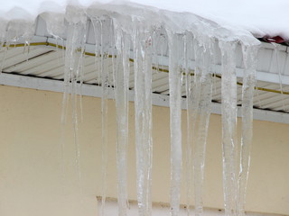 Beautiful icicles on the roof of a stone house in the city - drops, thaw, spring in the urban area