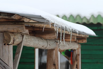 Icicles on the roof of a old wooden house in the village - thaw, spring in the countryside