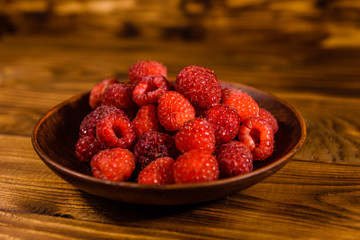Ceramic plate with ripe raspberries on wooden table