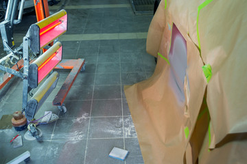 Infrared drying of car body parts after applying putty and paint on a red off-road vehicle in the body repair shop with red lanterns in the working environment