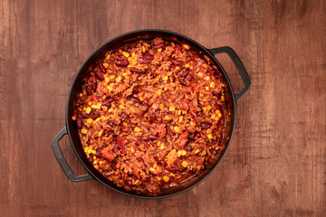 A large cast iron pan with chili con carne, shot from above on a dark rustic wooden table with a place for text