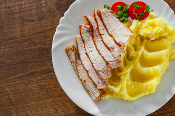 meat slices with mashed potatoes in white plate on wooden table background