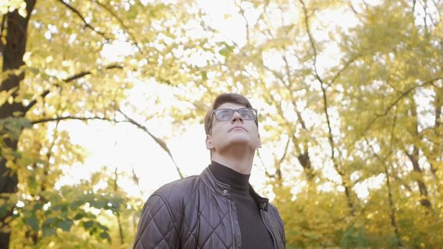 Young man with glasses looks around in the autumn park