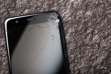 Smartphone with broken glass on display and copy space on a stone surface