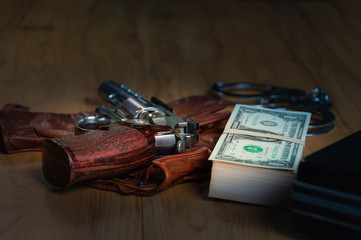 Obraz premium Dollar banknotes, shackles, document bag and carbiines put on gloves on a wooden table, to Dark business concept.