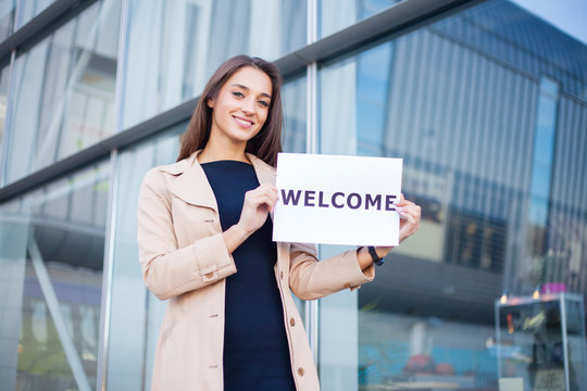 Businesswoman With Long Hair Holding A Sign Board With A Welcome Has Airport Background