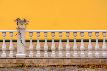 White Railing with columns and a vase for flowers. The wall is painted with yellow paint.
