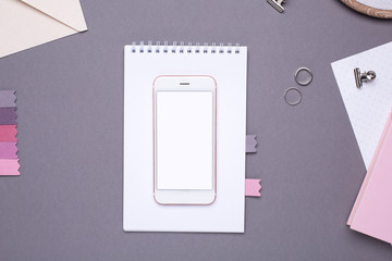 Mobile phone with empty screen with white notepad and embroidery on grey background