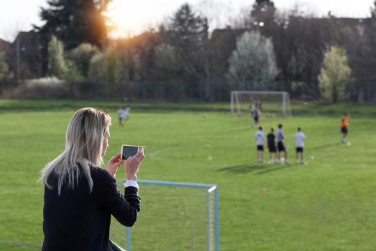 Mother Watching Or Taking Photo Of Her Son Playing Football. Sport, Tailgating, Active Lifestyle, Happy Family Concept