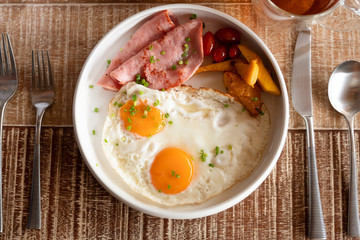 Breakfast with eggs, tomatoes , mushrooms, ham, bacon and herbs top view over the wooden table