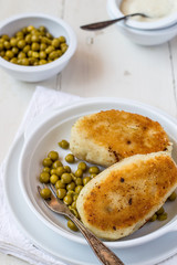 Potato cutlet with mushroom filling and canned green peas on a round white plate on an old table. 