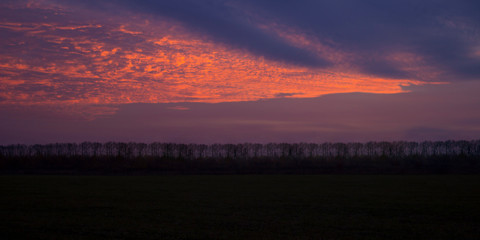 Dramatic valley sky sunset panoramic mountain landscape background.level forest on the horizon.Cumulus sunset clouds with sun setting down on dark background.orange cloud sky and blue sky. Cumulus sun