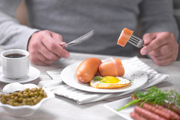 Obraz na płótnie Canvas мужчина ест сосиску с яичницей и свежей зеленью