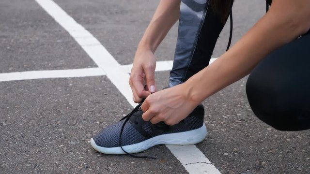 Girl runner tying laces for jogging her shoes on road in a park. Sport lifestyle.