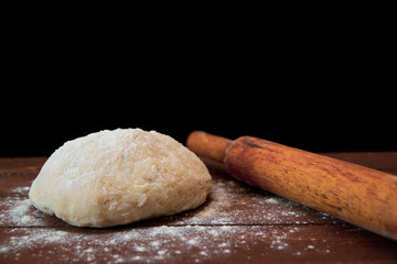 a lump of dough and a rolling pin lie on a wooden table on a black background