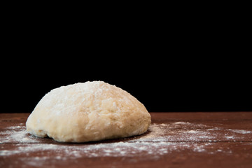 Fototapeta na wymiar a lump of dough lie on a wooden table on a black background
