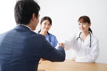 握手する男性ビジネスマンと女性医師　見守る看護師