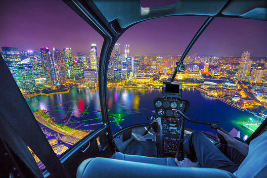 Scenic helicopter flight above Singapore skyline at dawn. Night urban aerial scene. cockpit interior with financial district skyscrapers at night on Singapore harbor.