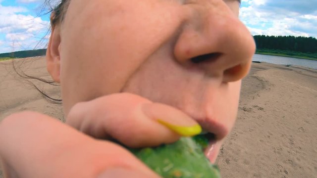 The girl eagerly taking a bite of the cucumber and eats it with great pleasure