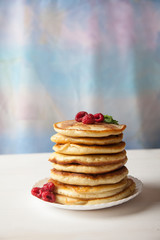 Pancakes with raspberries stacked on a white plate