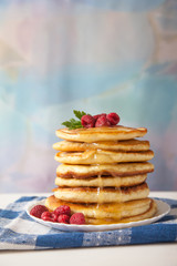 pancakes with raspberries and honey lie on a plate on a blue napkin