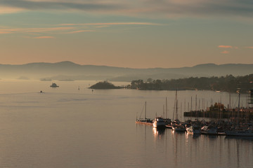 Sunset in Oslo, Norway. Panorama of the evening coast. Mountain landscape on the horizon. Lighthouse and sailing boats on a colorful sunset