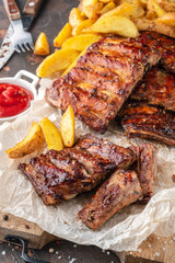 Delicious barbecued ribs on an rustic wooden chopping board with potato wedges and sauce