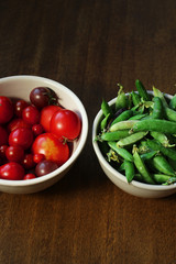top view of organic home grown vegetables in clay bowls on a brown wooden table