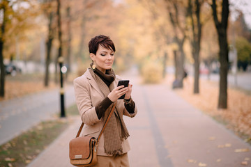 stylish young woman uses smartphone against background of autumn street
