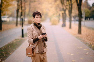 stylish young woman uses smartphone against background of autumn street