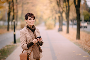 stylish young woman uses smartphone against background of autumn street