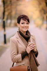 stylish young woman uses smartphone against background of autumn street