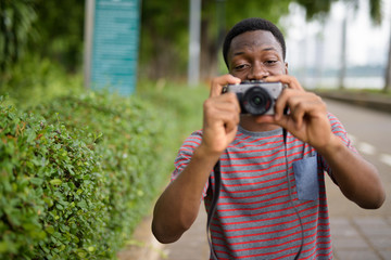 Young handsome African man taking pictures with camera in park