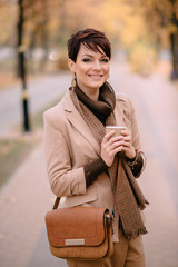 portrait of a young female with cup coffee in her hands against background of autumn street