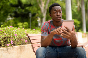 Fototapeta premium Young handsome African man using digital tablet in park