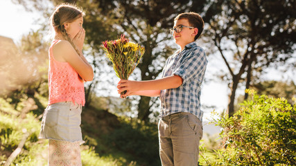 Naklejka na ściany i meble Boy giving a bouquet of flowers to his girlfriend in a park