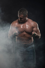 muscular man training with a harness on a black background in smoke