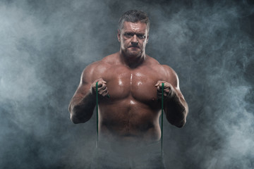 Fototapeta na wymiar muscular man training with a harness on a black background in smoke